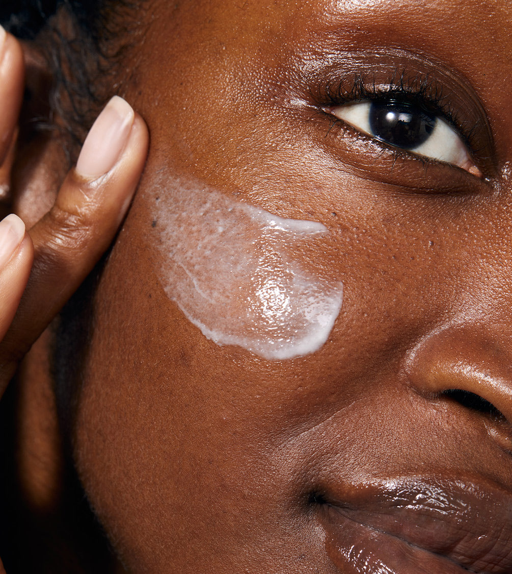 A close up of model's face applying Gold Night Drops.