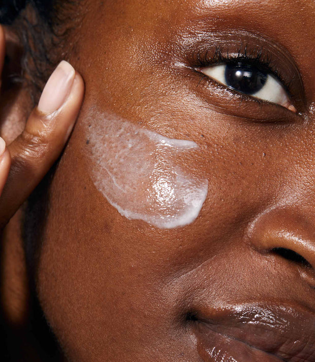 A close up of model's face applying Gold Night Drops.