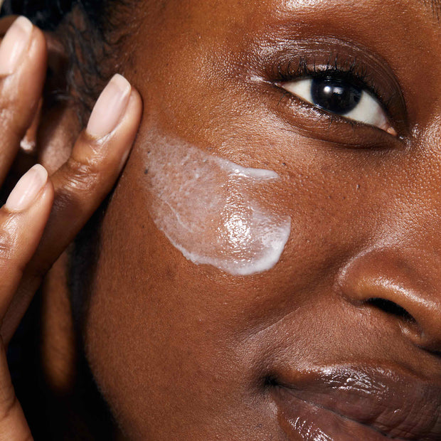 A close up of model's face applying Gold Night Drops.