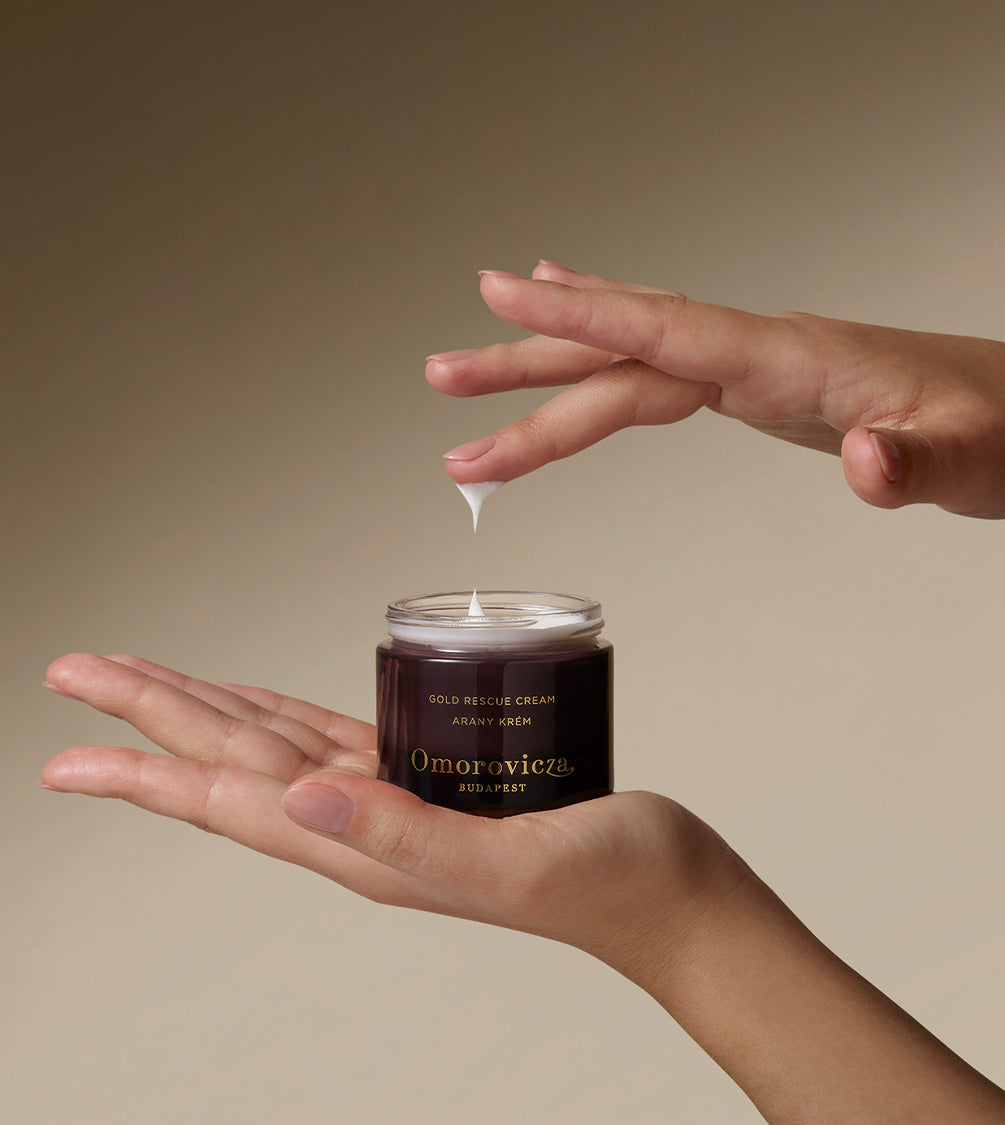 Hands holding Gold Rescue Cream. Picking up a little bit of product with a finger.