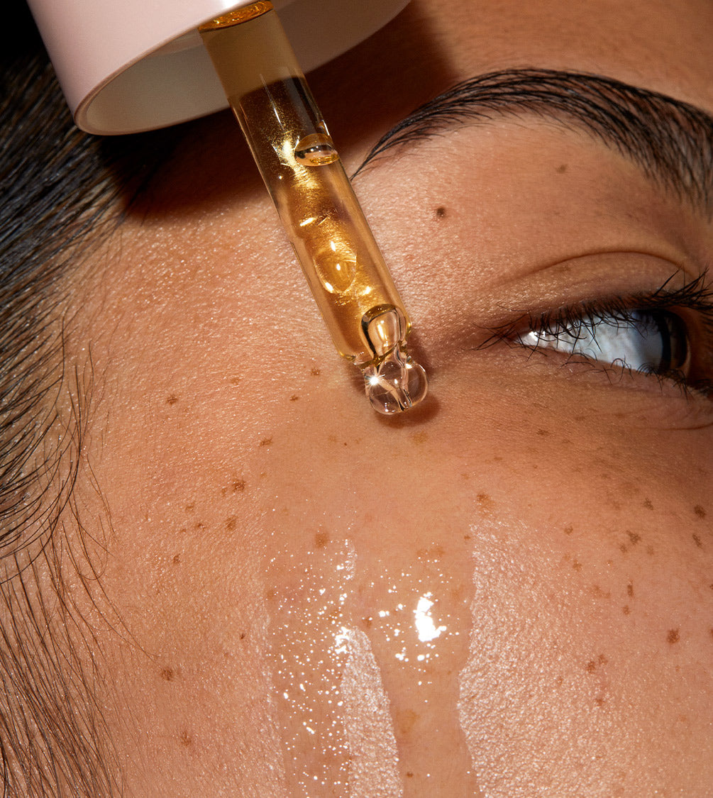 A super close up of model's face Queen oil is applied to her skin with a pipette. The skin is glowy and hydrated.