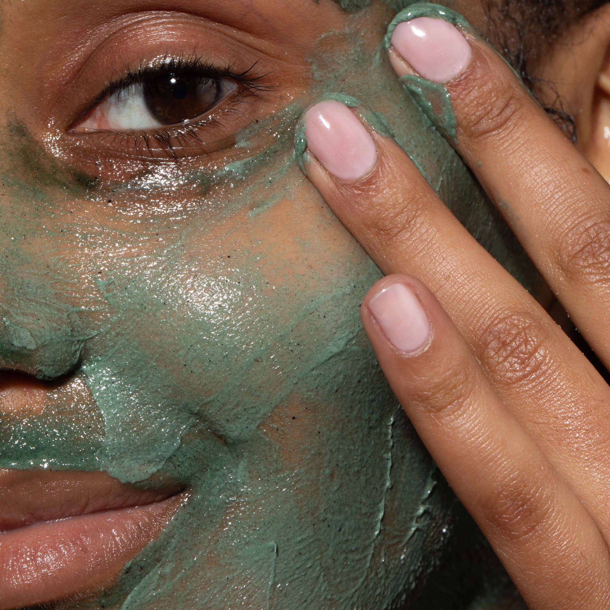 A close up of model's face with Refining Facial Polisher applied to her skin. Designed to brighten dull, lacklustre skin.